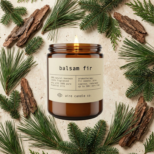 Balsam fir candle from aire candle co surrounded by pine needles, cedarwood bark, cypress and fir pieces on a light travertine background.