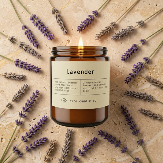 lavender candle from aire candle co surrounded by lavender sprigs on a light travertine background.