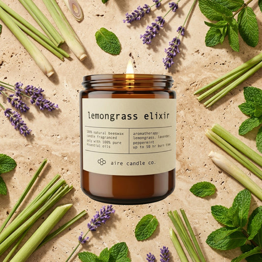 lemongrass elixir candle from aire candle co surrounded by lemongrass stalks, lavender and peppermint on a light travertine background.