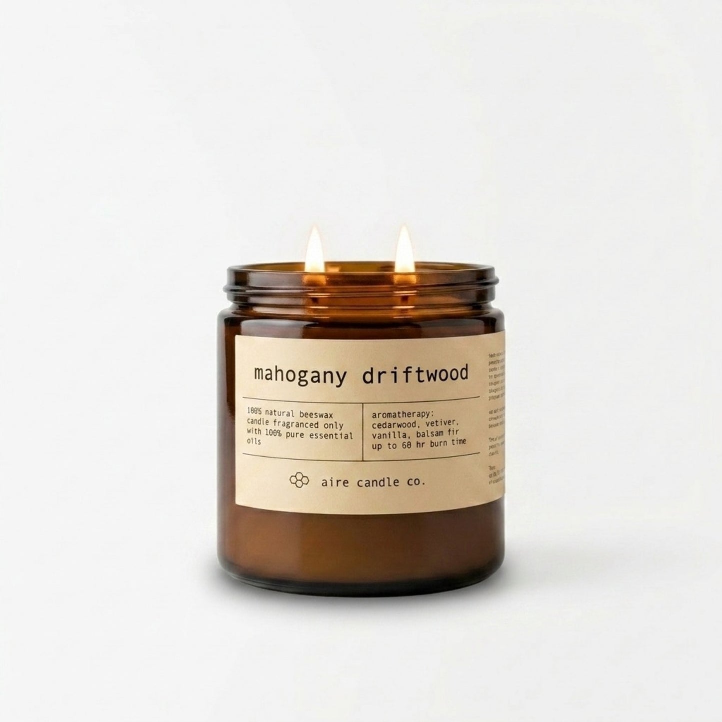 16 oz mahogany driftwood scented beeswax candle by aire candle co. in an amber jar showing two wicks illuminated and a label on a white background