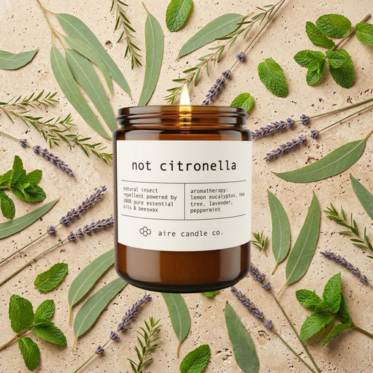 Aire Candle Co. 'not citronella' outdoor beeswax candle surrounded by lemon eucalyptus, peppermint, lavender and tea tree on a travertine background