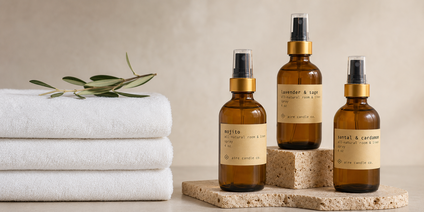 A collection of Aire Candle Co. all-natural room sprays housed in amber glass jars. The room sprays are sitting next to a cleanly folded group of towels.