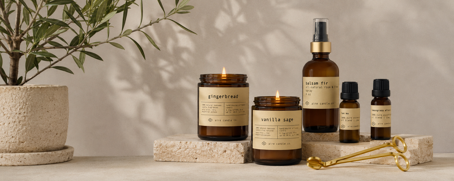 aire candle co. products featuring the gingerbread and vanilla sage candles, balsam fir room spray, essential oils and wick trimmer on travertine platforms in a modern, minimalistic setting. All-natural products housed in amber glass jars.
