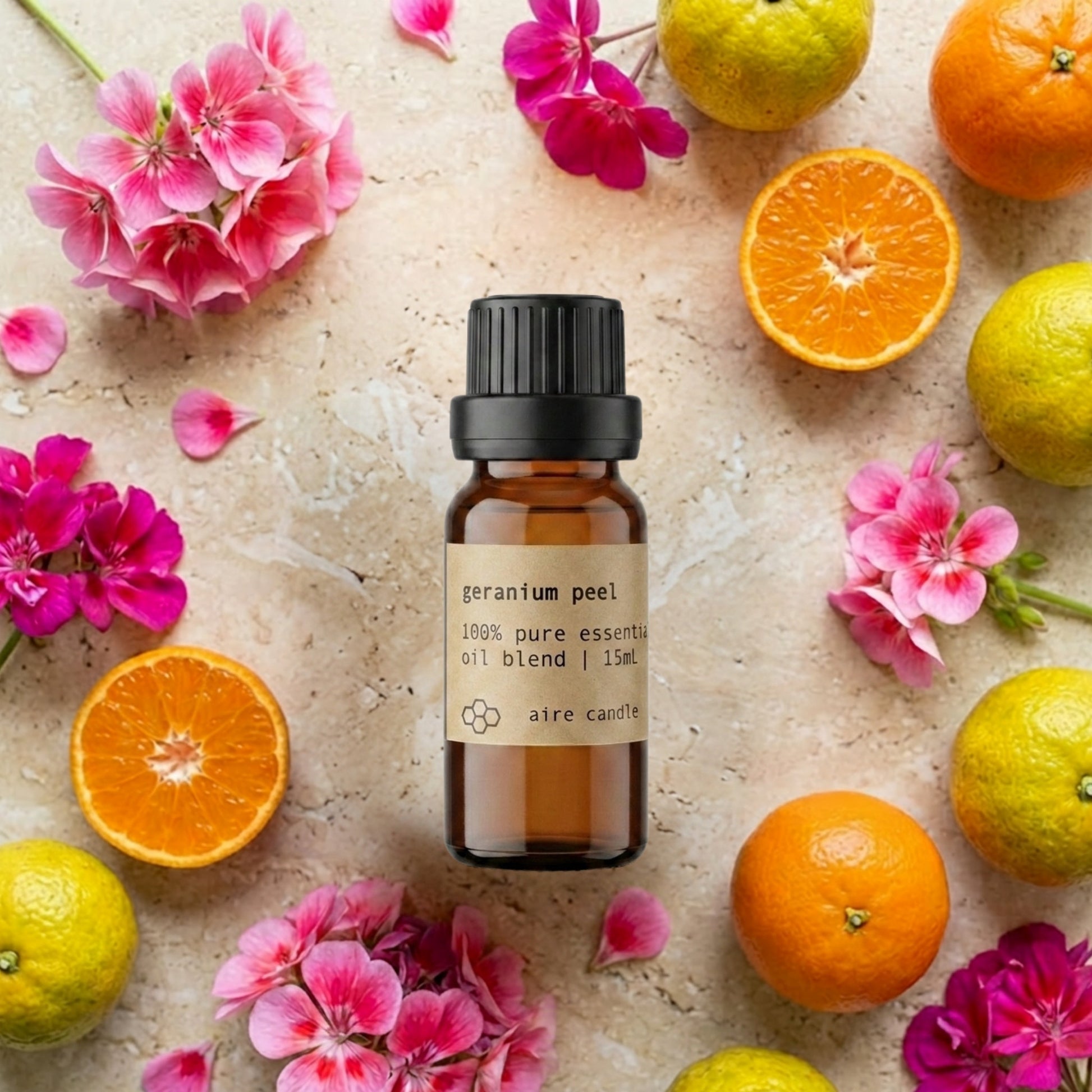 Bottle of Aire Candle Co. Geranium Peel Essential Oil Blend Surrounded by Scent Notes of Geranium, Clementine and Bergamot Essential Oils on a Travertine Surface.