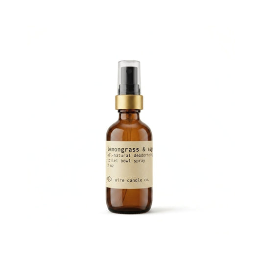 Aire Candle Co. Lemongrass & Sage Essential Oil Scented Deodorizing Toilet Bowl Spray Displayed Against a Clean White Background Housed in a Protective Amber Glass Bottle with a Gold Rim and Black Fine Mist Sprayer.