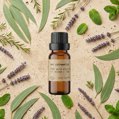 Bottle of Aire Candle Co. Not Citronella Essential Oil Blend Surrounded by Scent Notes of Insect Repelling Essential Oils of Lemon Eucalyptus, Peppermint, Tea Tree and Lavender on a Travertine Surface.