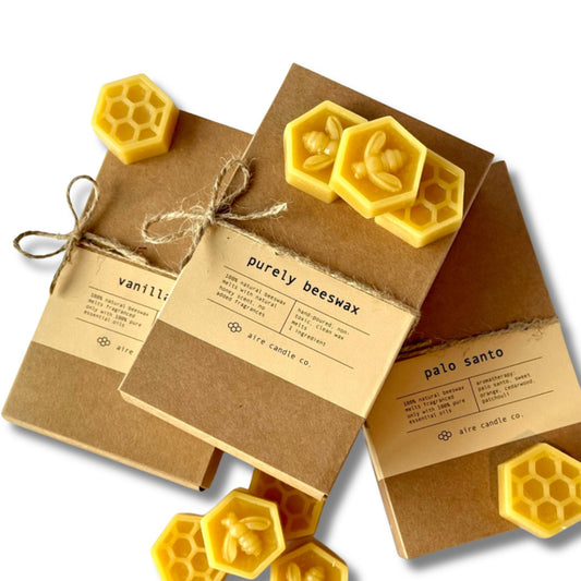 Aire candle co. stacked wax melt boxes featuring purely beeswax, vanilla sage and palo santo scents with beeswax tarts scattered across.