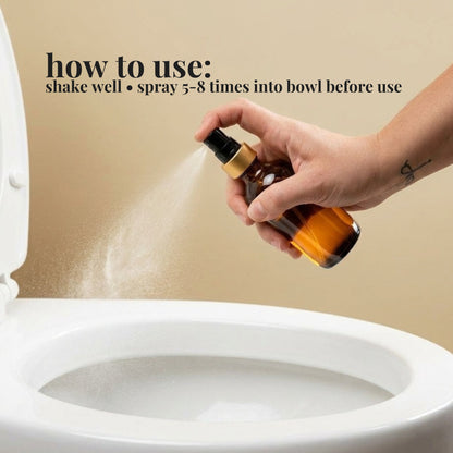 Hand holding a Sweet Orange & Clove toilet bowl spray bottle over a toilet bowl with usage instructions on a beige background. How to use: shake well & spray 5-8 times into bowl before use.