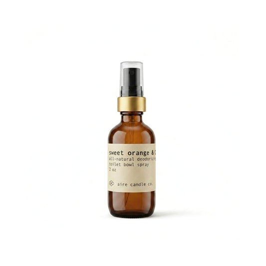 Aire Candle Co. Sweet Orange & Clove Essential Oil Scented Deodorizing Toilet Bowl Spray Displayed Against a Clean White Background Housed in a Protective Amber Glass Bottle with a Gold Rim and Black Fine Mist Sprayer.
