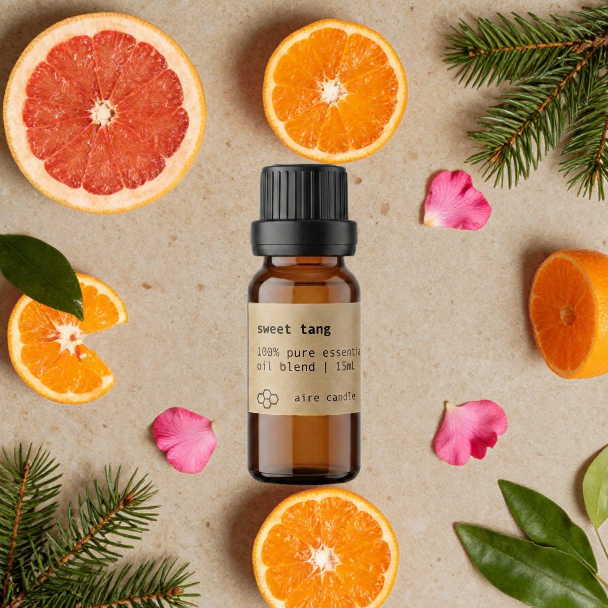 Bottle of Aire Candle Co. Sweet Tang Essential Oil Blend Surrounded by Scent Notes of Tangerine, Grapefruit, Spruce and Geranium Essential Oils on a Travertine Surface.