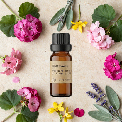 Bottle of Aire Candle Co. Wildflowers Essential Oil Blend Surrounded by Scent Notes of Geranium, Yland Ylang, Clary Sage and Lavender Essential Oils on a Travertine Surface.