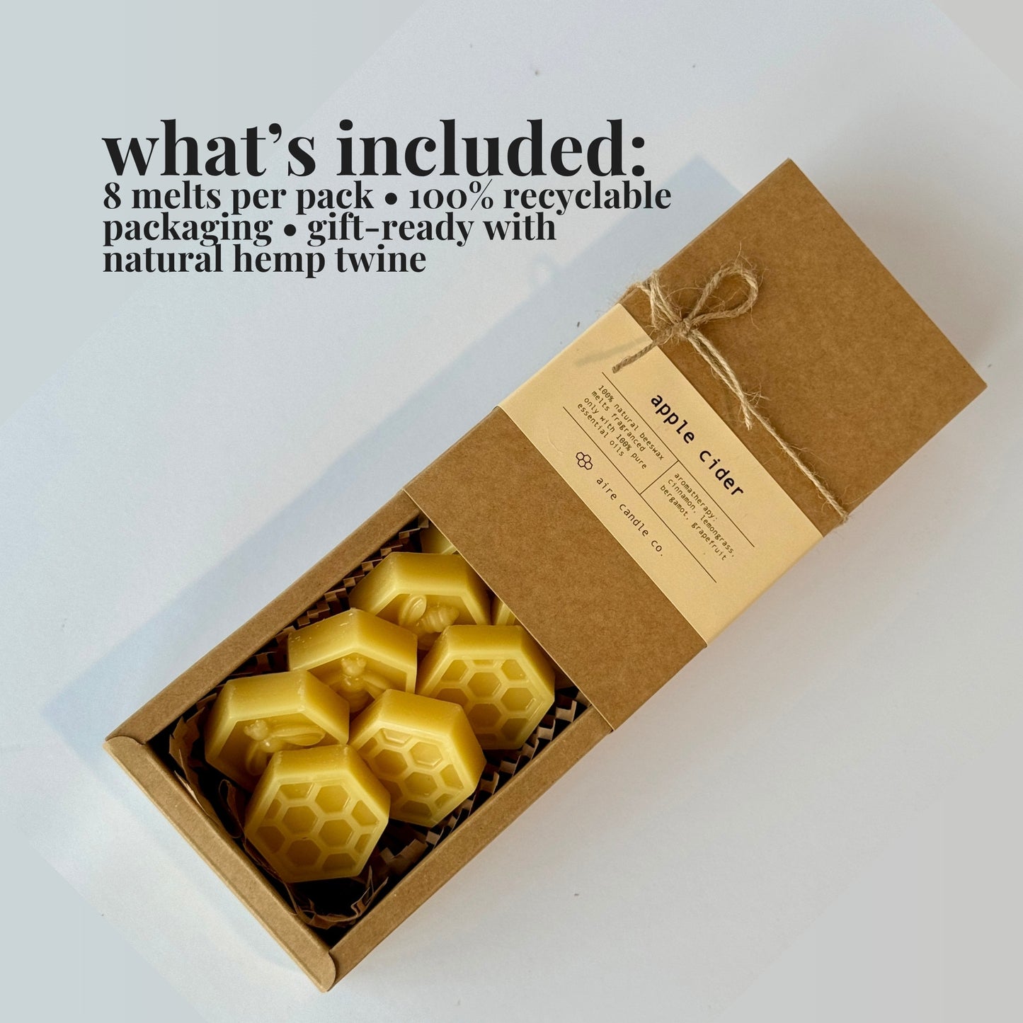 An open kraft paper gift box containing eight yellow honeycomb-shaped wax melts, with a kraft paper label tied with twine. Black text at the top reads 'what's included: 8 melts per pack • 100% recyclable packaging • gift-ready with natural hemp twine'.