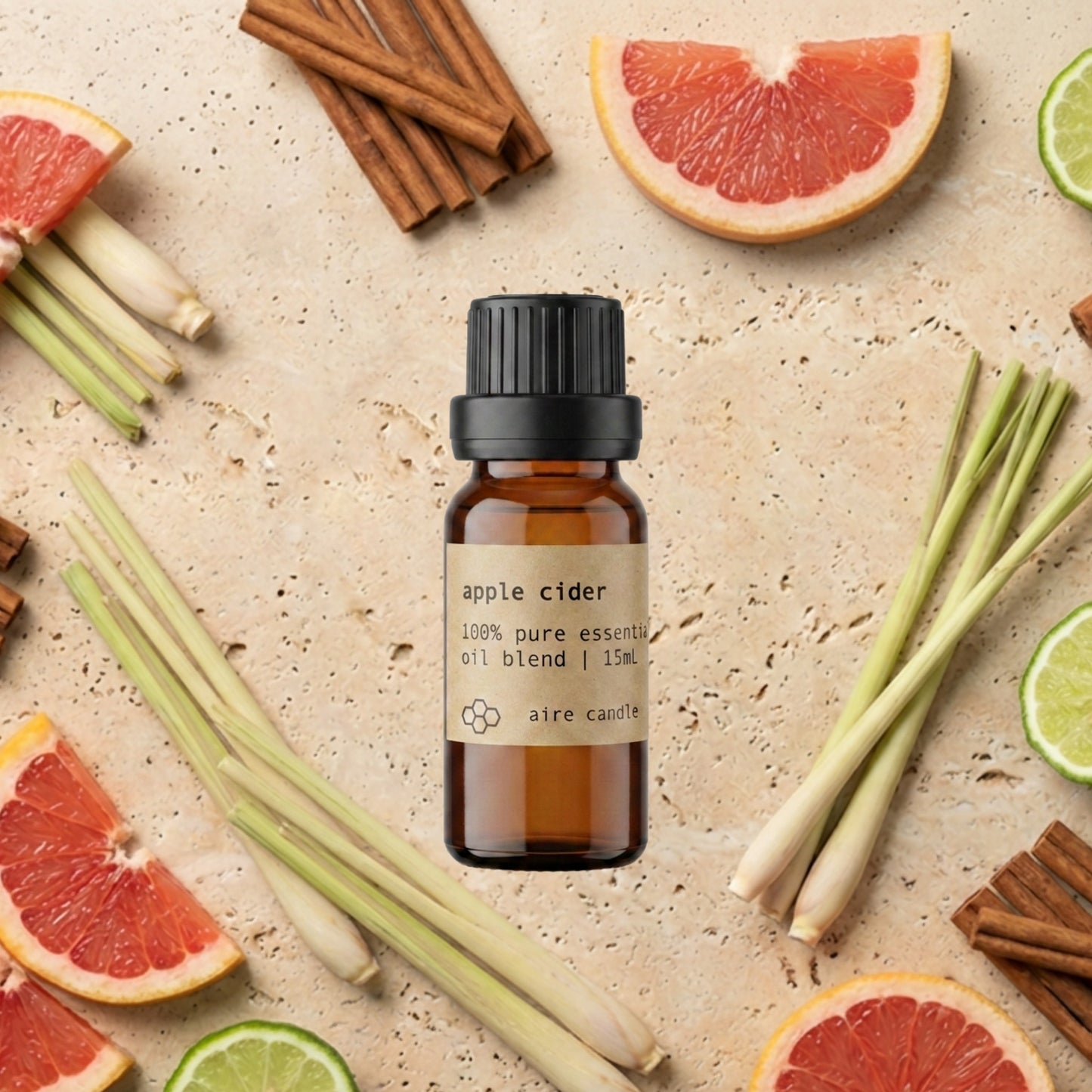 A small amber glass bottle of Aire Candle Co. 'apple cider' essential oil blend with a black cap, centered on a textured beige stone background and surrounded by grapefruit slices, lemongrass, cinnamon sticks, and bergamot wedges.