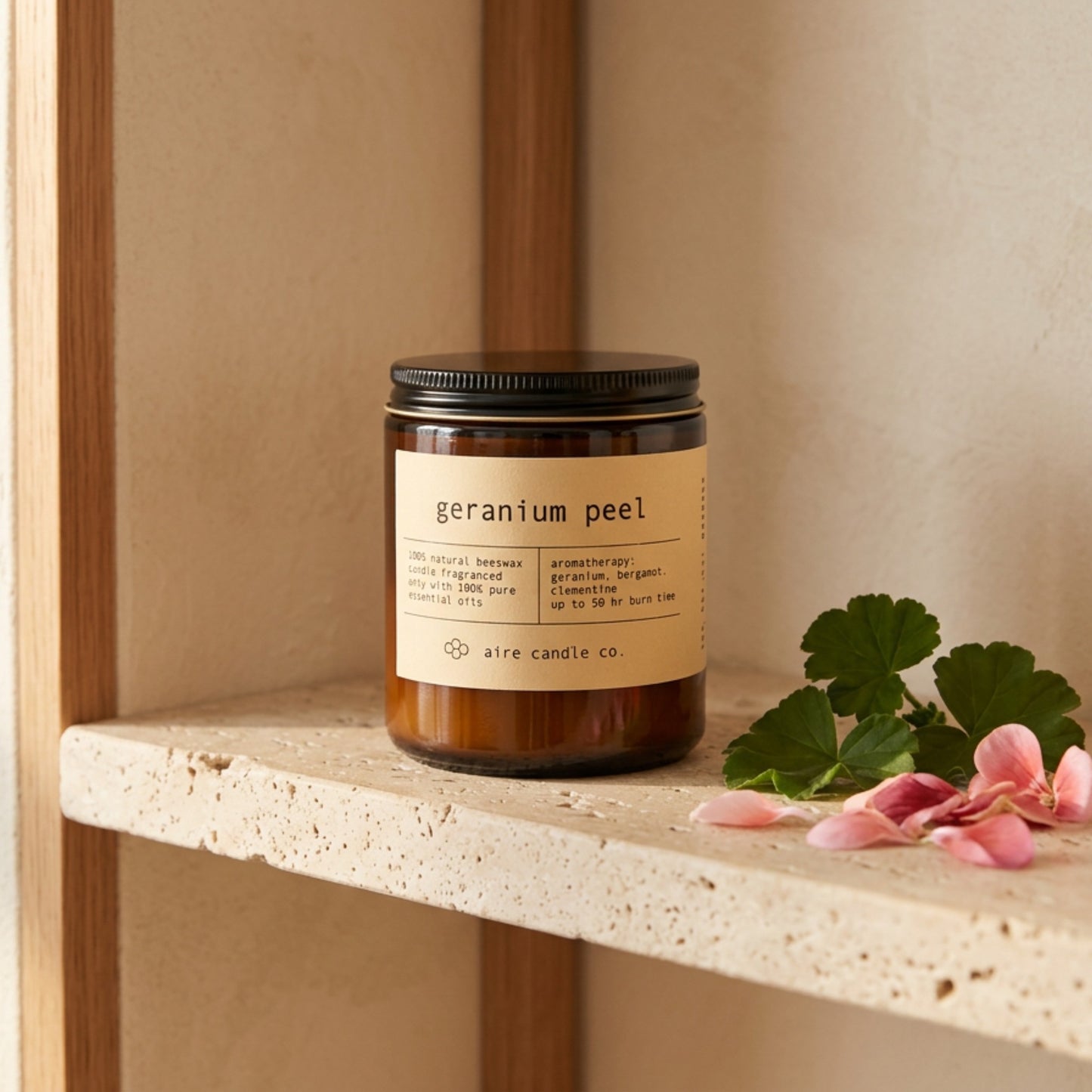 Candle labeled 'geranium peel' by aire candle co. on a travertine shelf.
