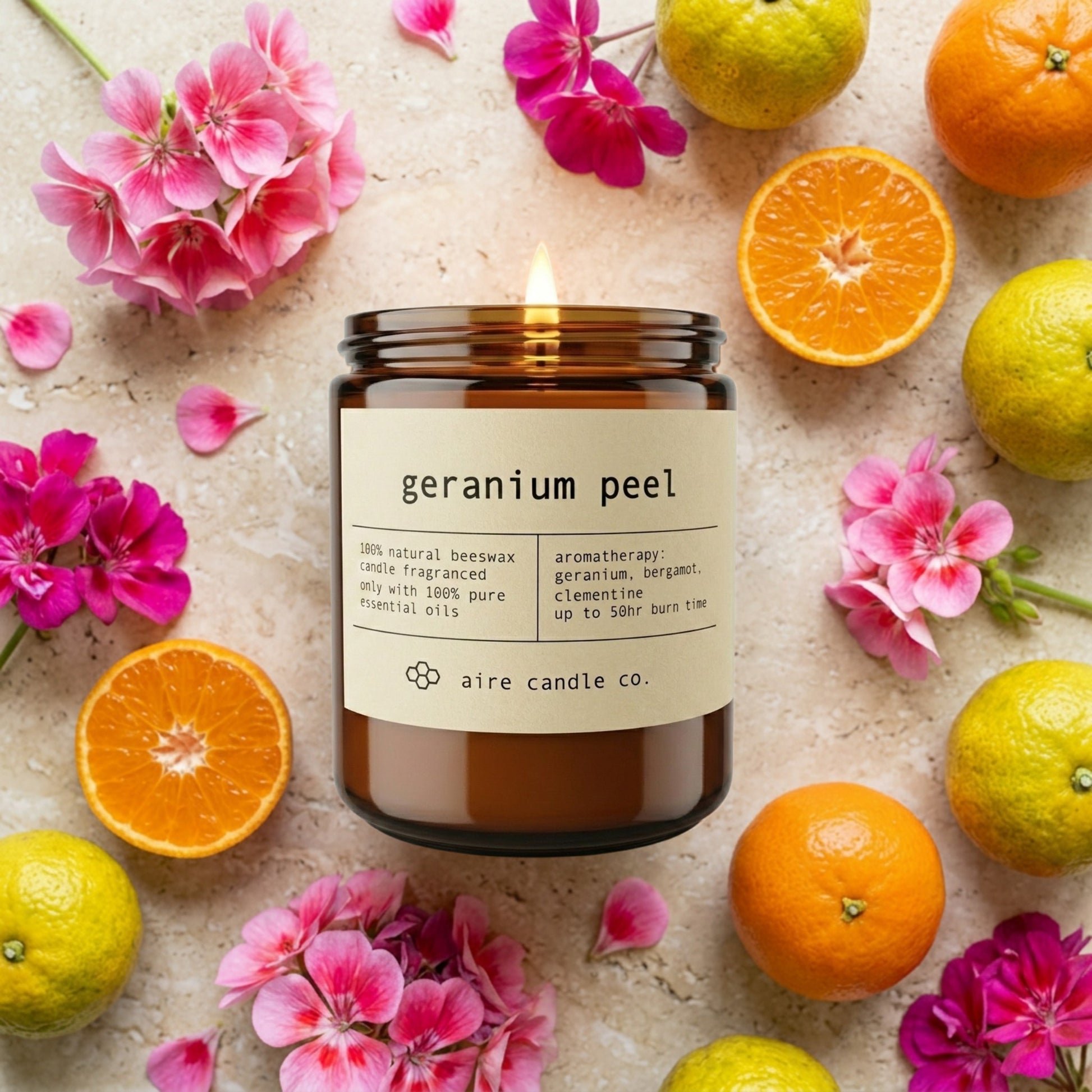 Geranium Peel candle from aire candle co surrounded by geranium flowers, clementines and bergamots on a light travertine background.