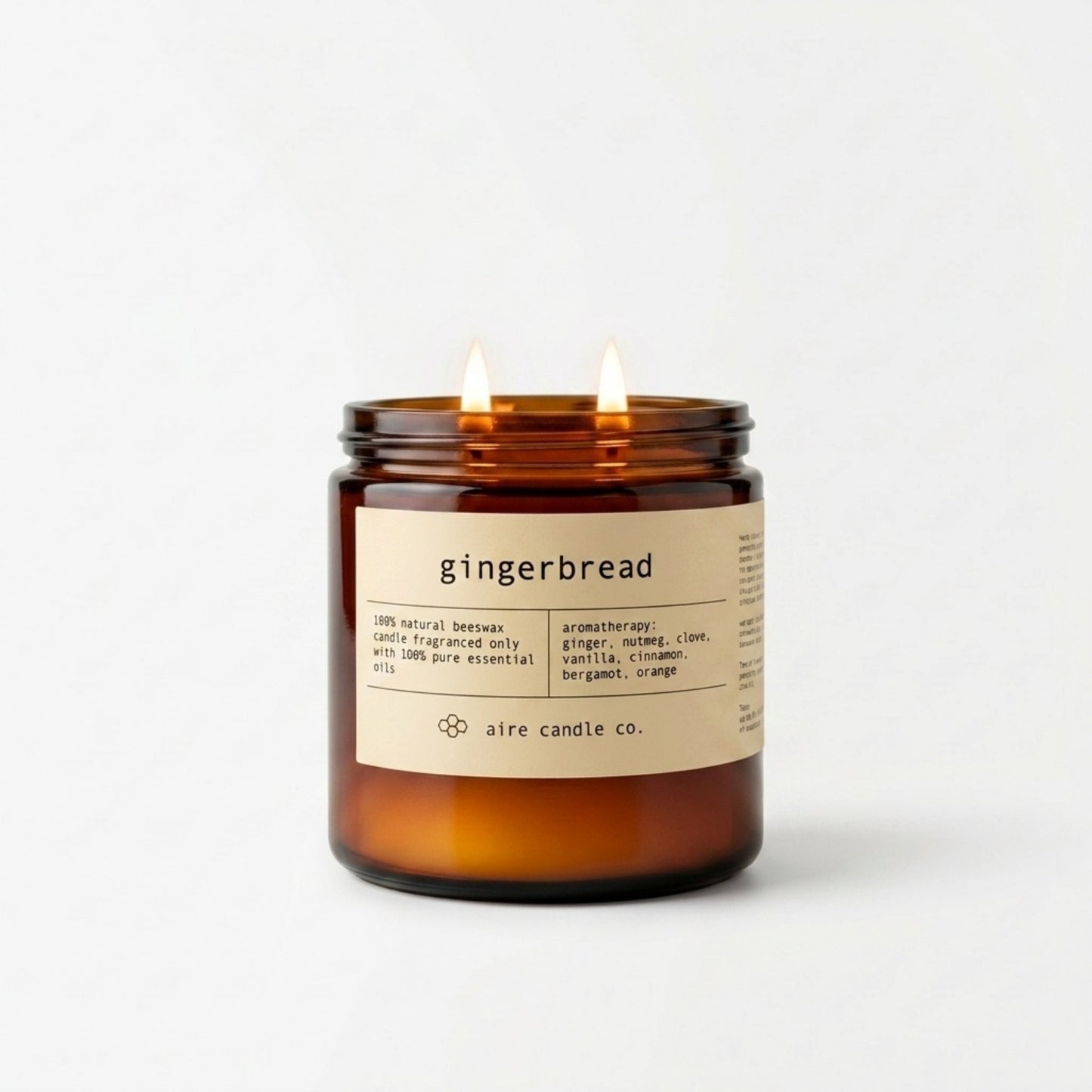 16 oz gingerbread candle by aire candle co. in an amber jar showing two wicks illuminated and a label on a white background