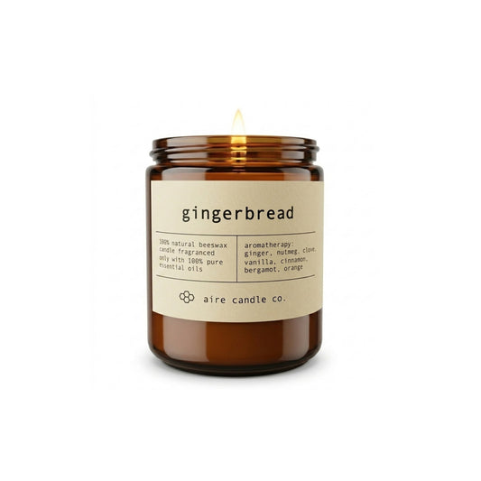 Aire Candle Co. Gingerbread Beeswax Candle Displayed with an Illuminated Flame Housed in a Protective Amber Glass Jar.