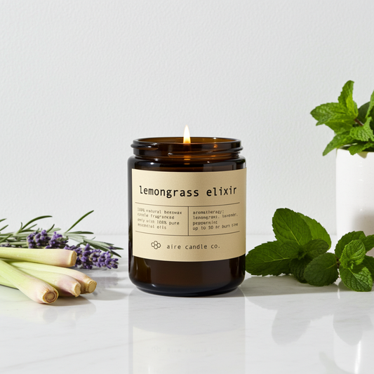 Lemongrass Elixir aromatherapy candle by Aire Candle Co. in an amber glass jar, burning on a sunlit surface with fresh lemongrass stalks, lavender sprigs, and mint leaves. This clean-burning beeswax candle is infused with essential oils, featuring a bright citrus lemongrass scent balanced with herbal and floral notes for a refreshing, spa-like home fragrance.