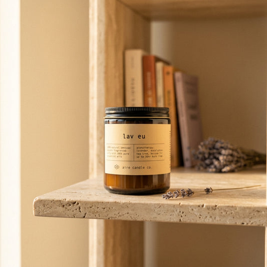 Candle labeled 'lav eu' by aire candle co. on a travertine shelf with books and lavender sprigs.