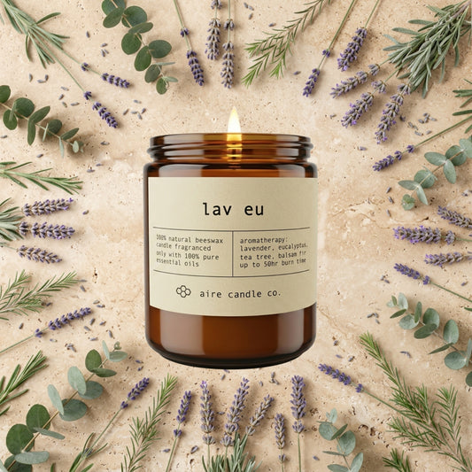 Lav Eu candle from aire candle co surrounded by lavender, eucalyptus, tea tree and balsam fir on a light travertine background.