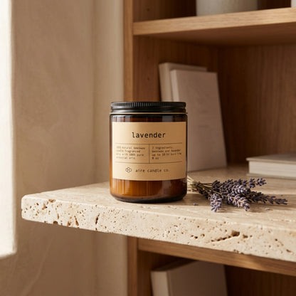Candle labeled 'lavender' by aire candle co. on a travertine shelf with lavender sprigs and books.