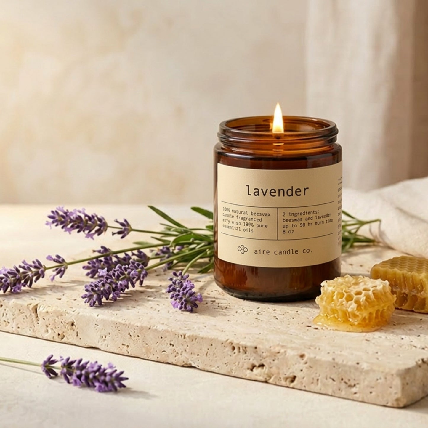 lavender candle by aire candle co. with natural elements of lavender and honeycomb on a travertine surface.