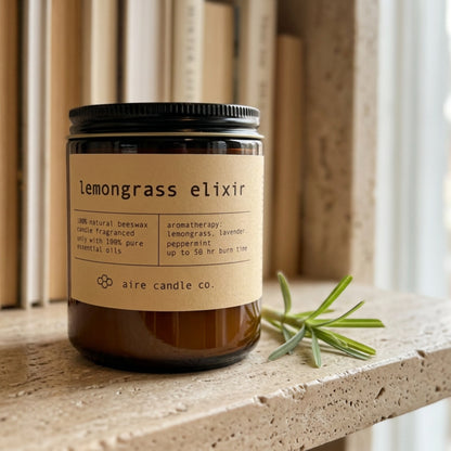 Candle labeled 'lemongrass elixir' by aire candle co. on a travertine shelf with books.