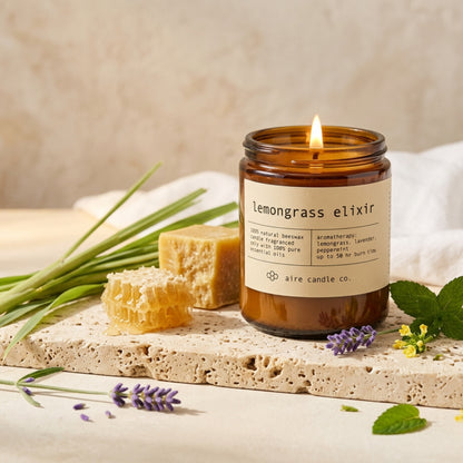 lemongrass elixir candle by aire candle co. with natural elements of lemongrass, lavender and peppermint on a travertine surface.