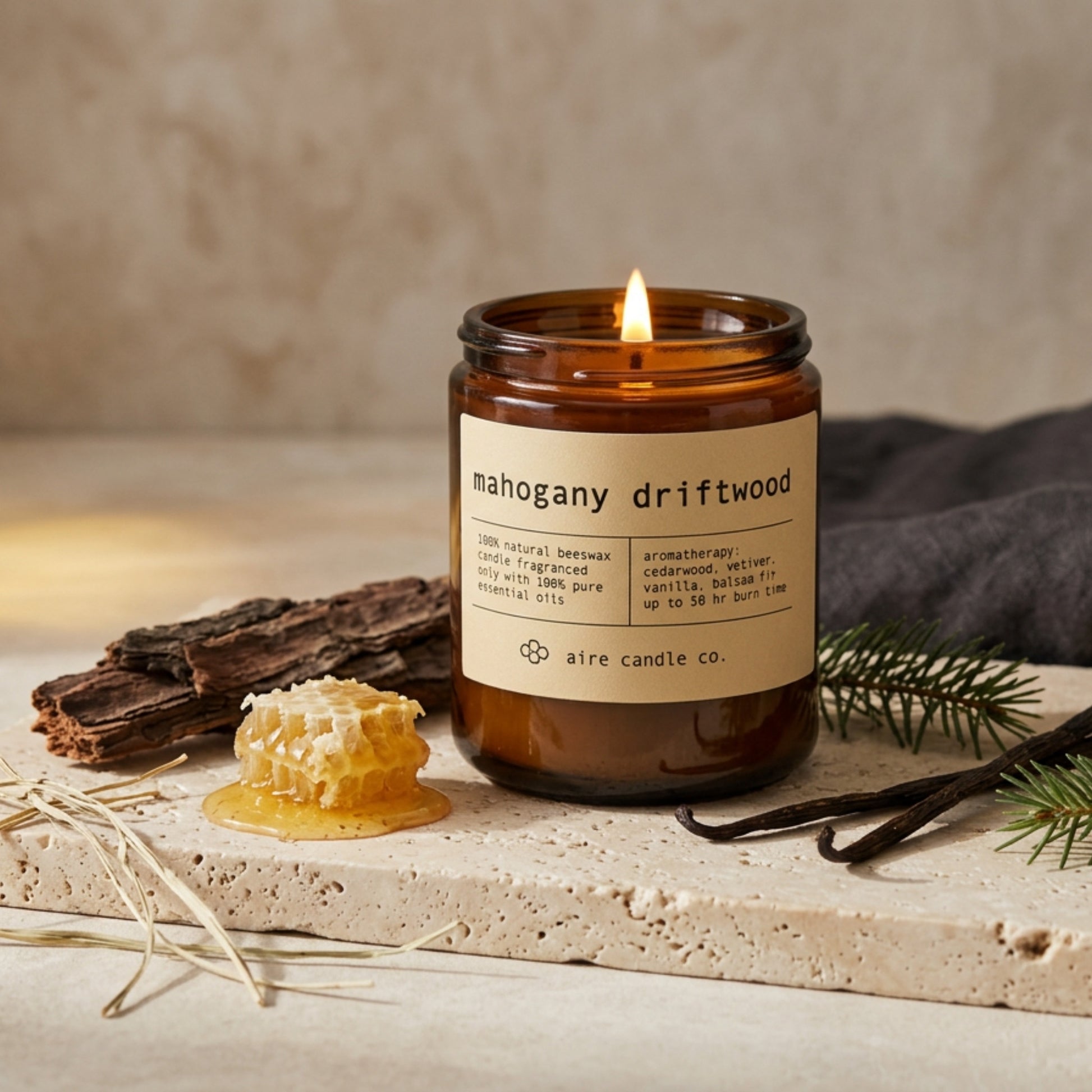 mahogany driftwood beeswax candle by aire candle co. with natural elements of honeycomb, cedarwood, balsam fir, vanilla and vetiver on a travertine surface.