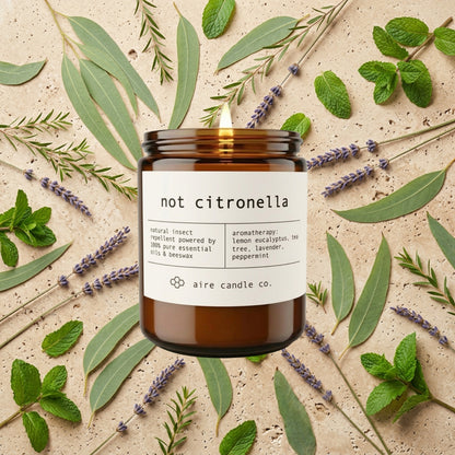 Aire Candle Co. 'not citronella' outdoor beeswax candle surrounded by lemon eucalyptus, peppermint, lavender and tea tree on a travertine background