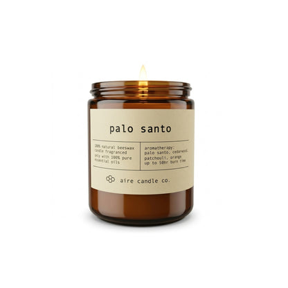 Aire Candle Co. Palo Santo Essential Oil Scented Beeswax Candle Displayed with an Illuminated Flame Housed in a Protective Amber Glass Jar.