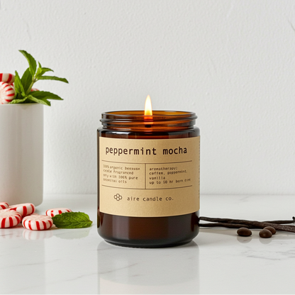 Aire Candle Co. peppermint mocha candle with a label on a white surface with peppermint candies and vanilla beans.