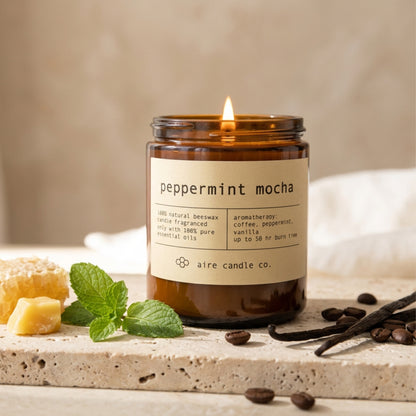peppermint mocha beeswax candle by aire candle co. with natural elements of honeycomb, peppermint, coffee beand and vanilla on a travertine surface.