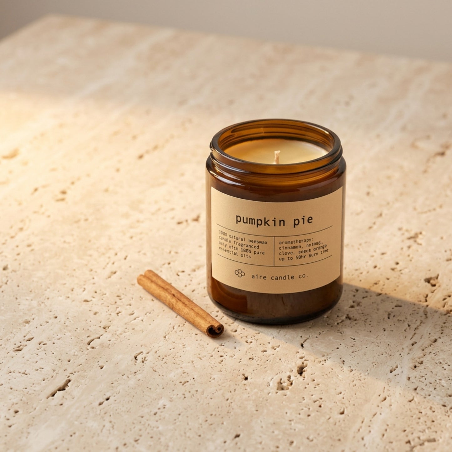 Amber glass candle labeled 'pumpkin pie' with a cinnamon stick on a stone surface