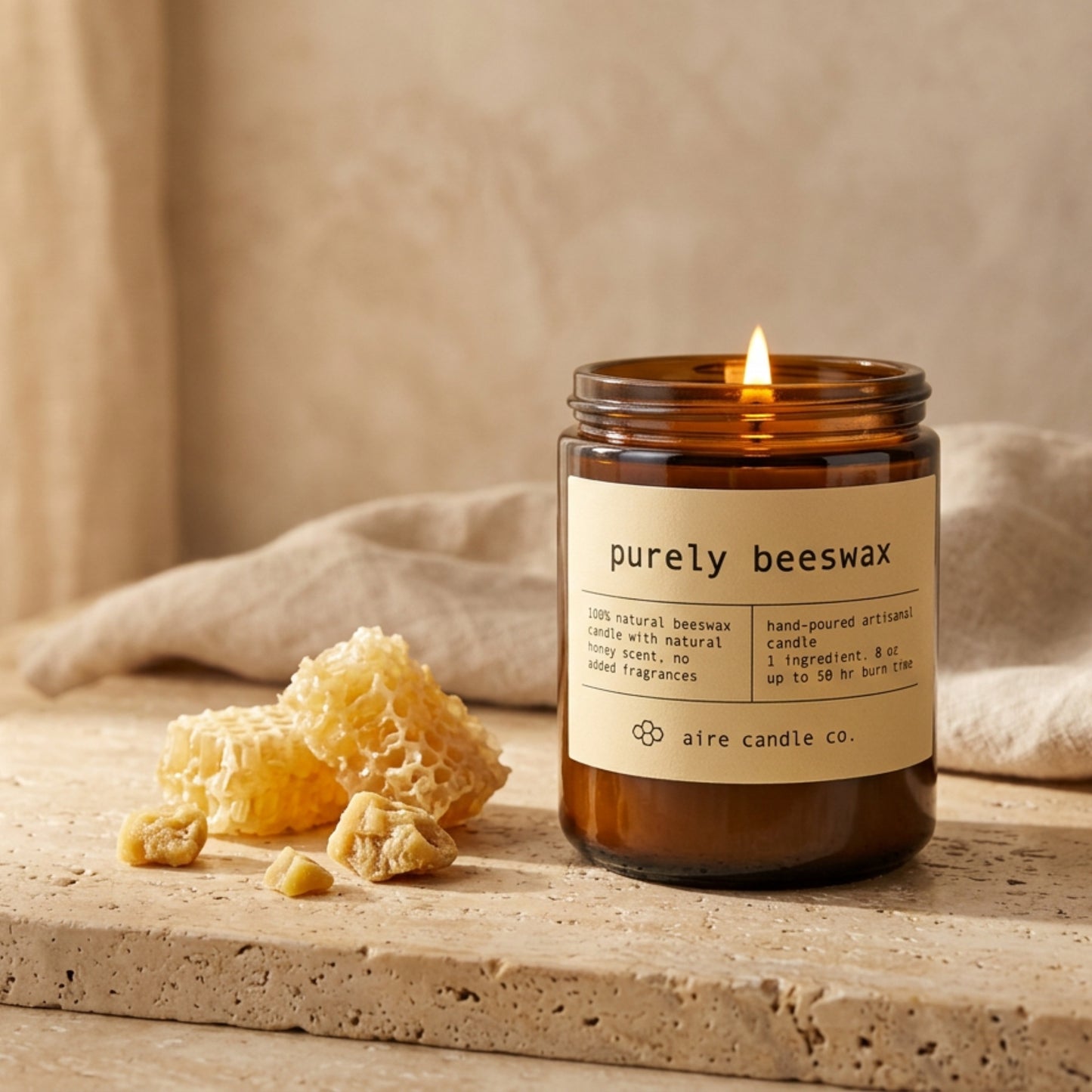 Purely beeswax candle in an amber jar with a label, surrounded by honeycomb and cloth on a travertine surface.