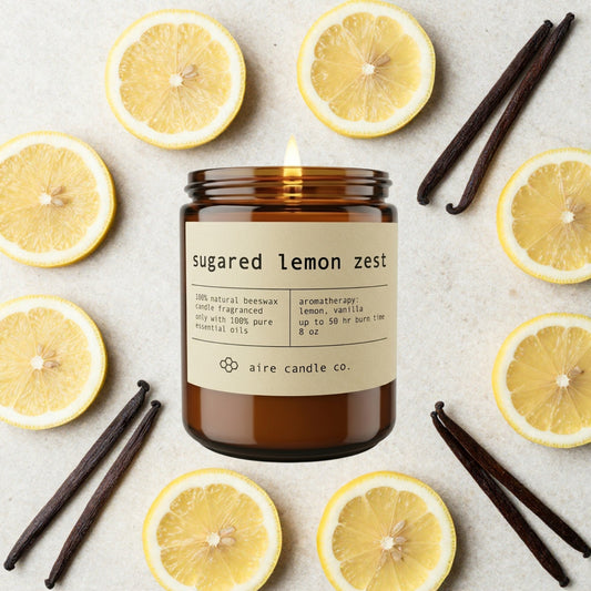 sugared lemon zest essential oil scented beeswax candle from aire candle co surrounded by lemons and vanilla beans on a light travertine background.