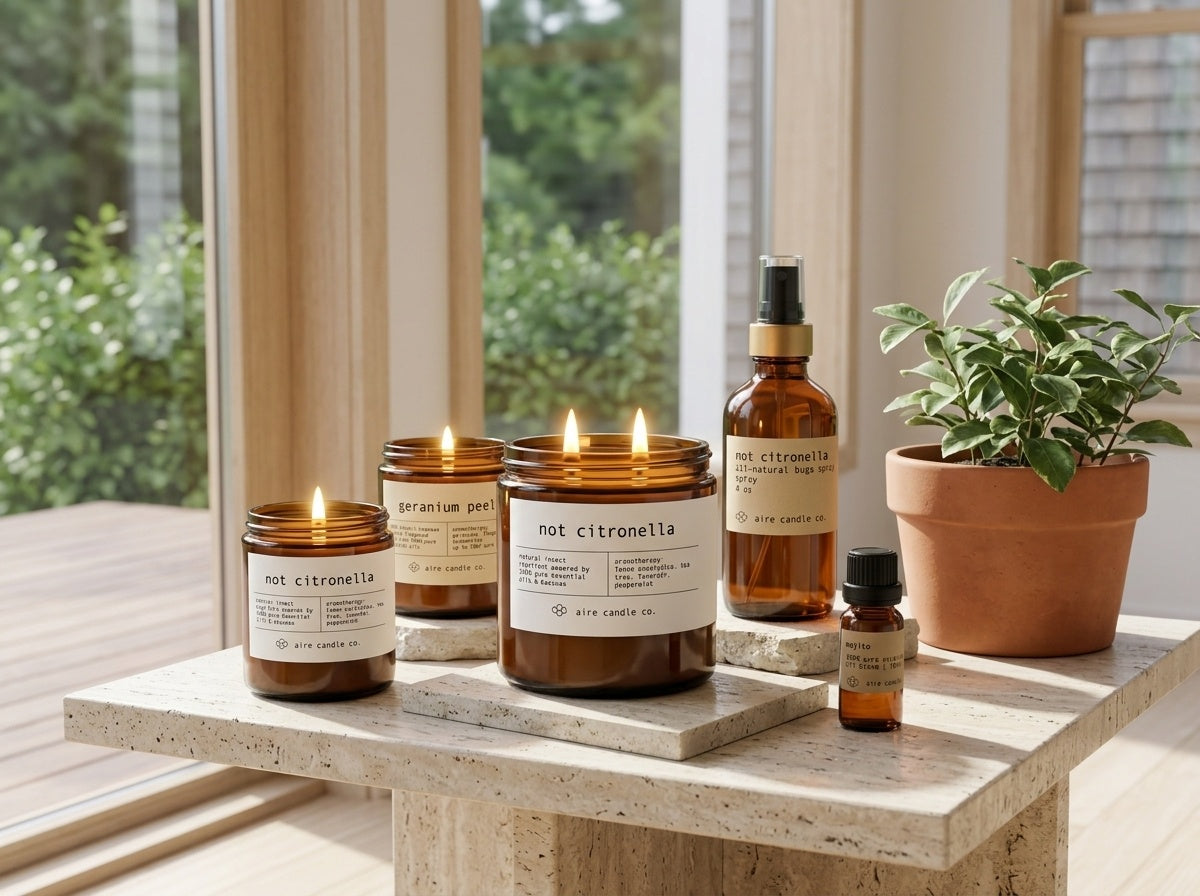 Aire Candle Co. Summer Collection featuring Not Citronella insect repellent candles, mojito essential oil, geranium peel candle and not citronella bug spray on a travertine table in an outdoorsy setting.