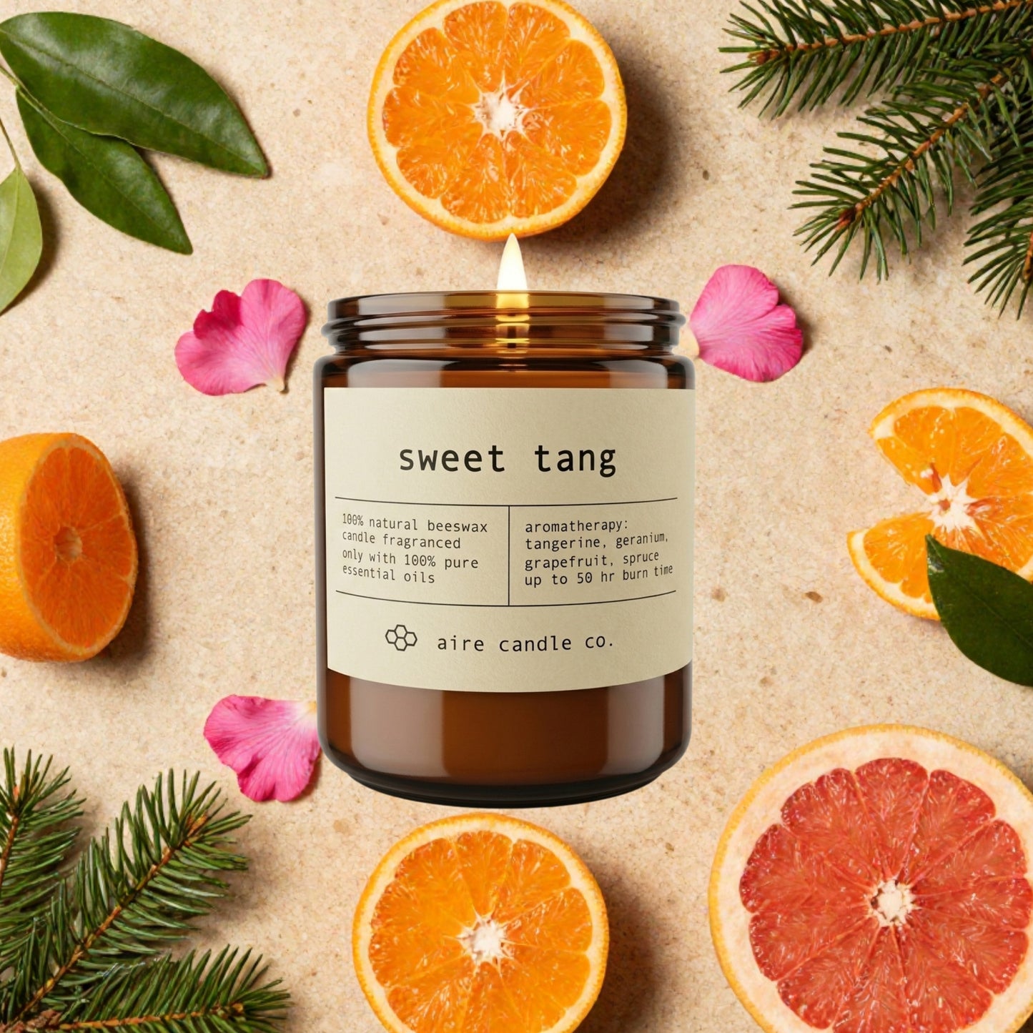 Aire Candle Co. 'Sweet Tang' candle surrounded by sliced tangerines, pink geraniums, grapefruit, and spruce needless on a textured surface.