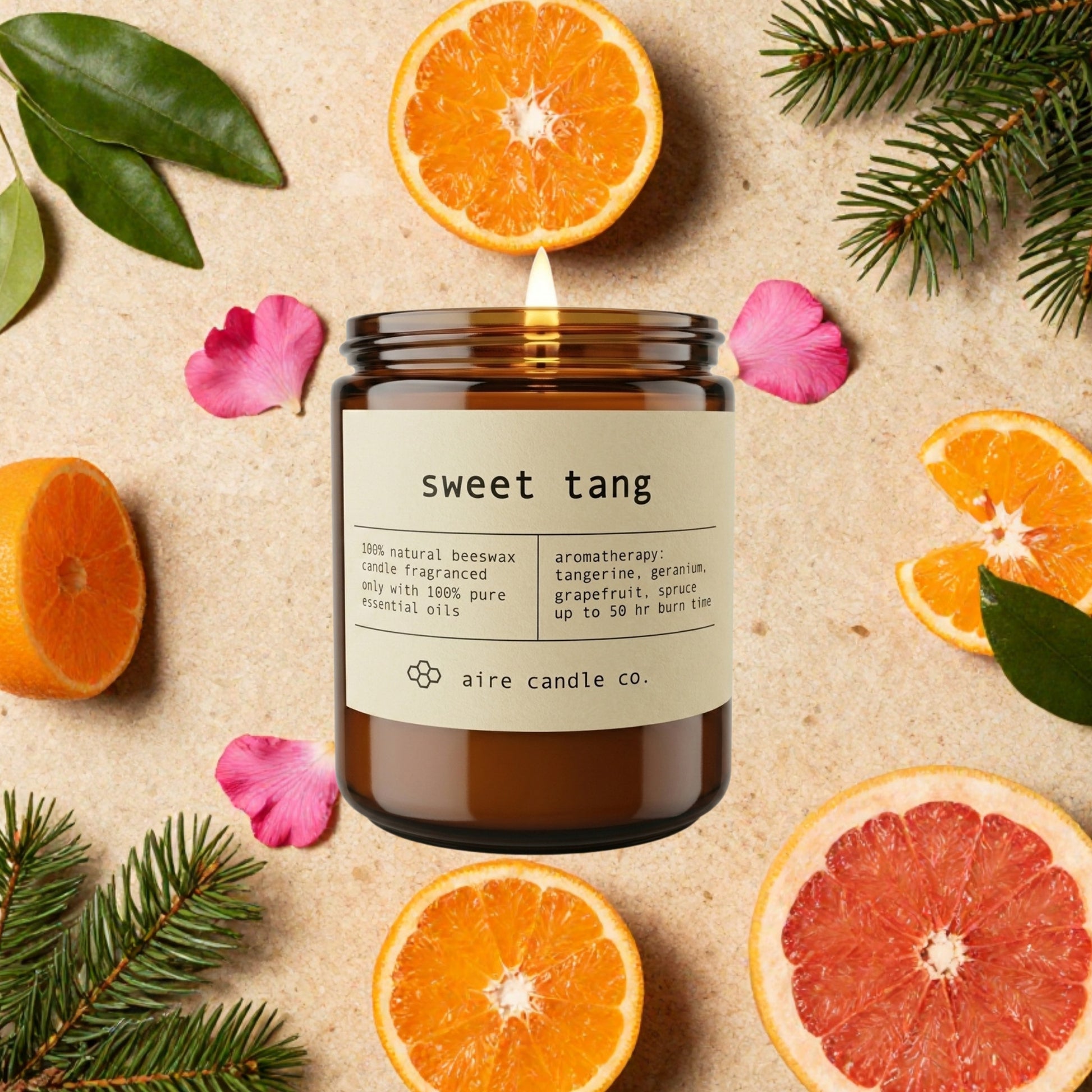 Aire Candle Co. 'Sweet Tang' candle surrounded by sliced tangerines, pink geraniums, grapefruit, and spruce needless on a textured surface.