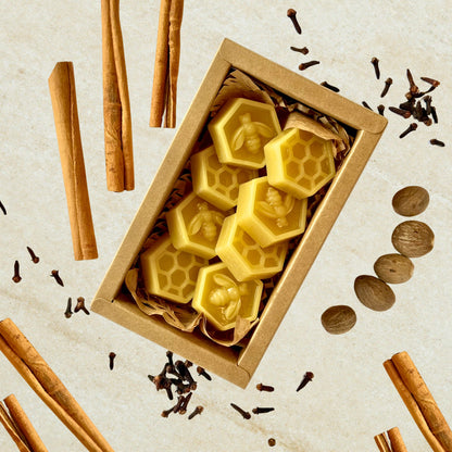 Hexagonal beeswax wax melts in a cardboard box with cinnamon sticks and cloves on a beige background