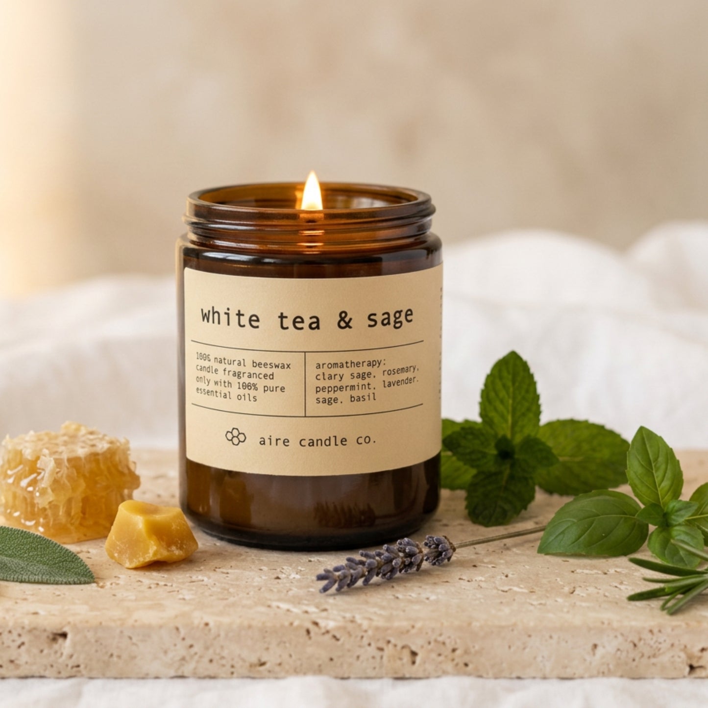white tea & sage beeswax candle by aire candle co. with natural elements on a travertine surface.