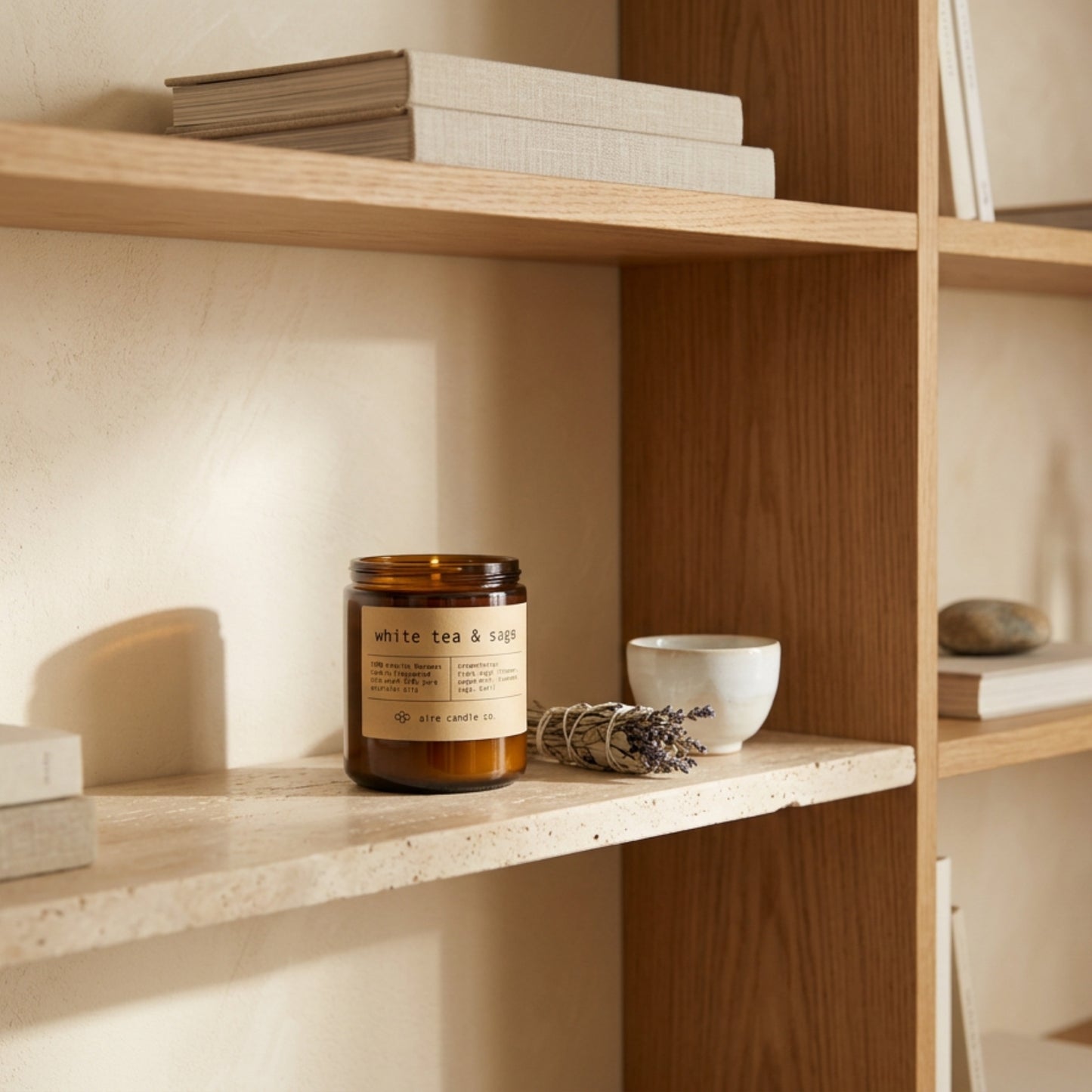 white tea & sage beeswax candle by aire candle co. with natural elements on a travertine surface next to a bundle of sage and lavender.