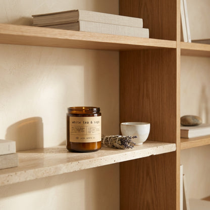 white tea & sage beeswax candle by aire candle co. with natural elements on a travertine surface next to a bundle of sage and lavender.