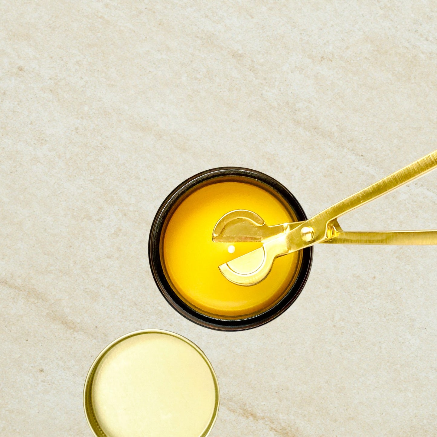 Gold wick trimmer by Aire Candle Co. hovering above an Aire Candle Co.'s beeswax candle's wick.