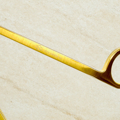 Gold wick trimmer on a beige textured background showcasing the aire candle co. engraving on the wick trimmer's handle.