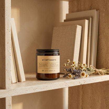 Candle labeled 'wildflowers' on a shelf with books and dried flowers